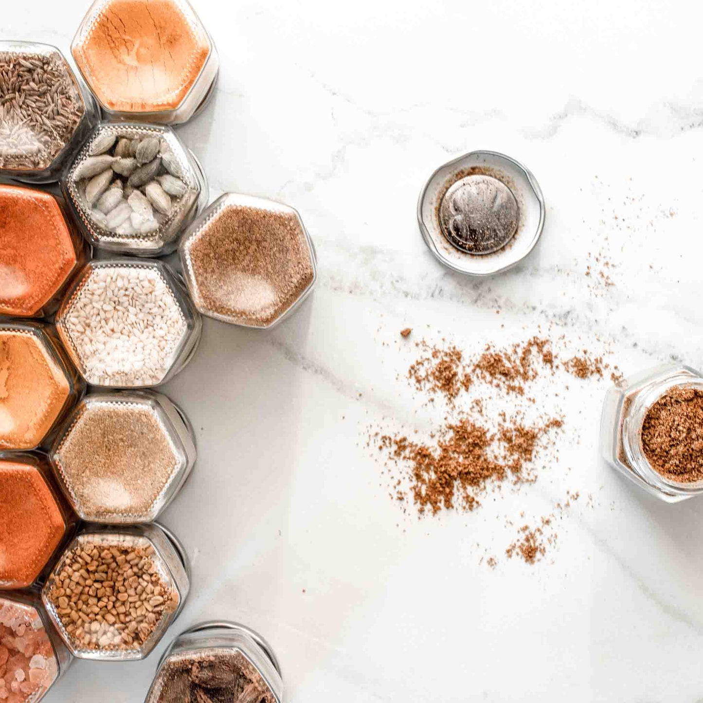 A set of spice jars facing down. There is one facing up with the lid off, showing the spice it holds and also the magnet attached to the lid