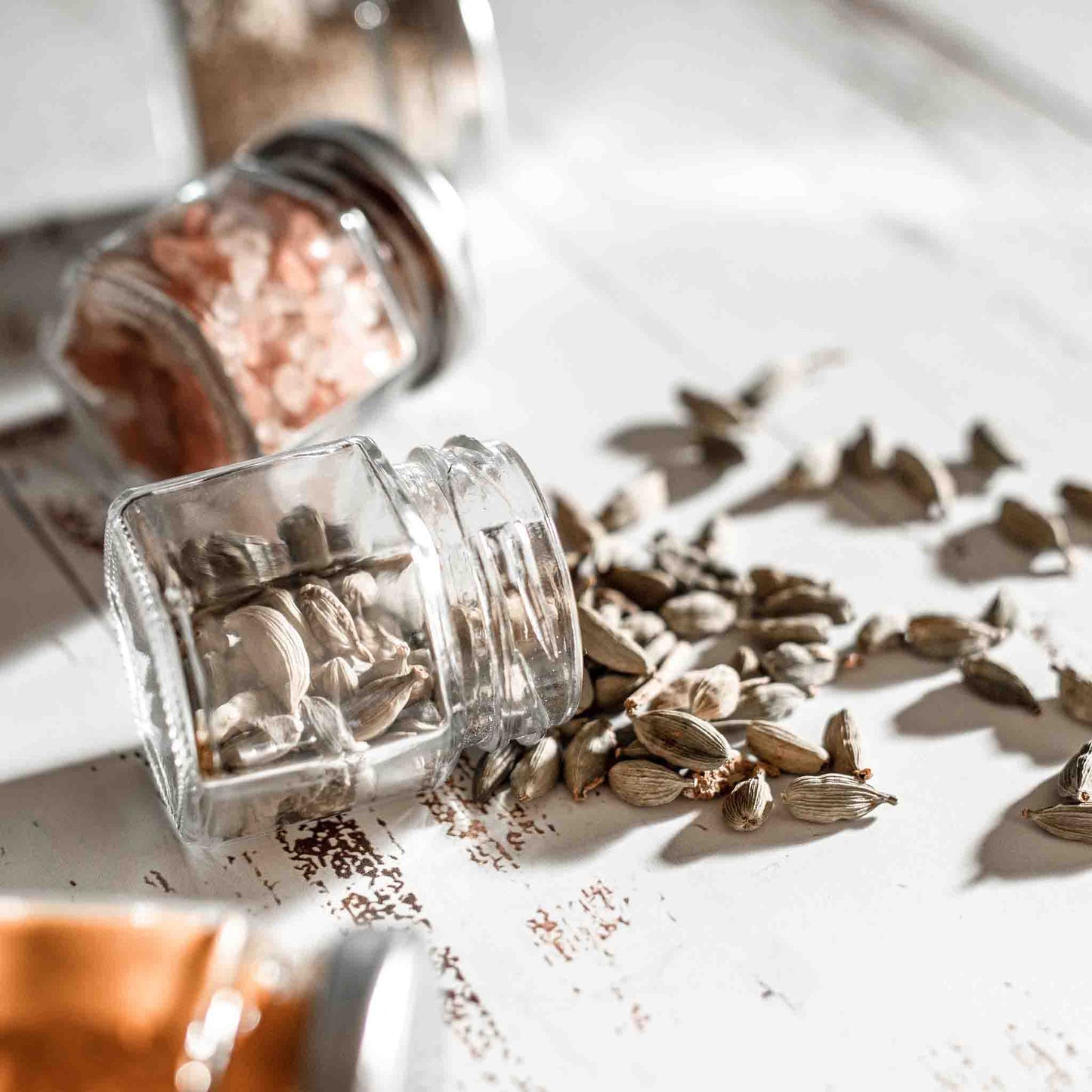 Three magnetic spice jars tipped over, with one open and showing cardamom seeds falling out